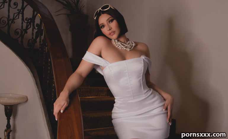 Real Mental Health Benefits Of Watching Hairy Cam Girls Glamour photo of a woman in a white off-the-shoulder dress posing on a curved staircase, wearing a chunky pearl necklace and sunglasses on her head.